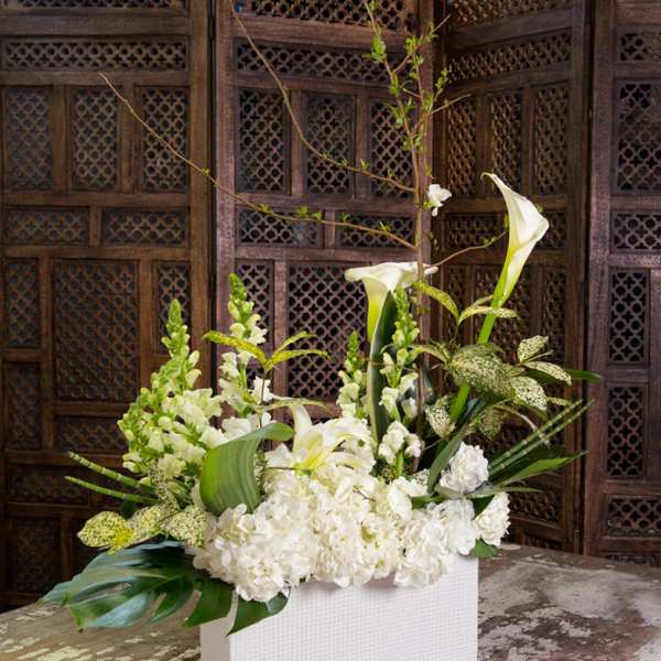 White floral arrangement with calla lilies and hydrangeas in a white rectangular vase