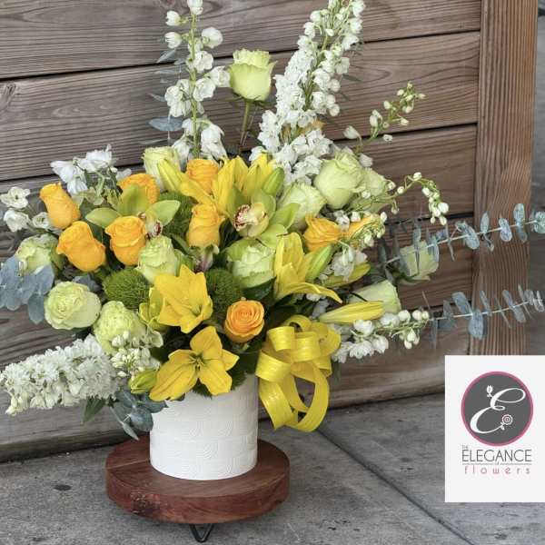Yellow and white floral arrangement in a white vase with a yellow ribbon