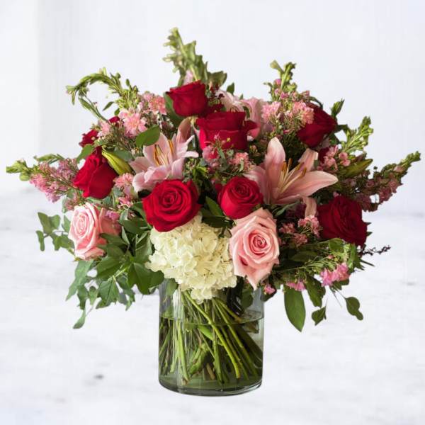 Arrangement of red and pink roses, pink lilies, and white hydrangea in a clear glass vase