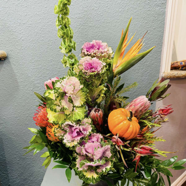 Tropical floral arrangement with pink and green blooms and a small pumpkin