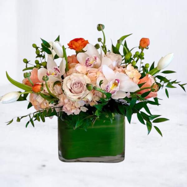 Low peach and white arrangement with roses, orchids, and tulips in a green-lined square glass vase
