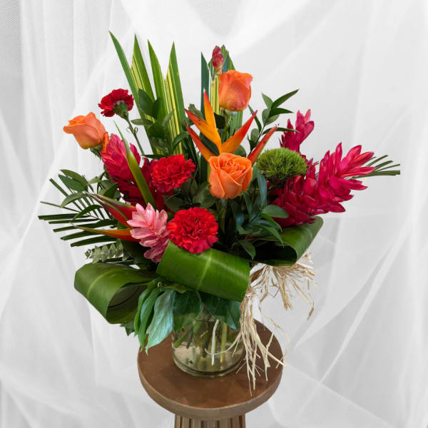 Tropical bouquet with orange roses, red carnations, and pink ginger flowers in a glass vase
