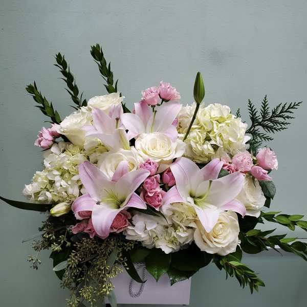 Pink lilies and white roses arranged in a white box with greenery