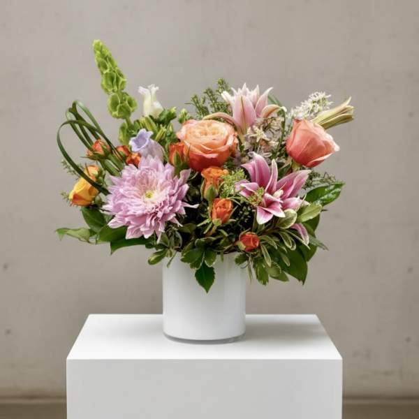 Mixed bouquet of pink, peach, and lavender flowers in a white vase