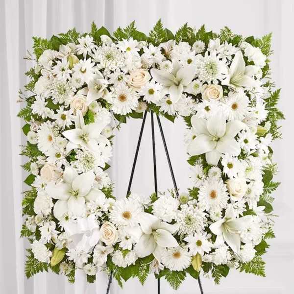 White floral wreath on a black easel with lilies, daisies, and roses