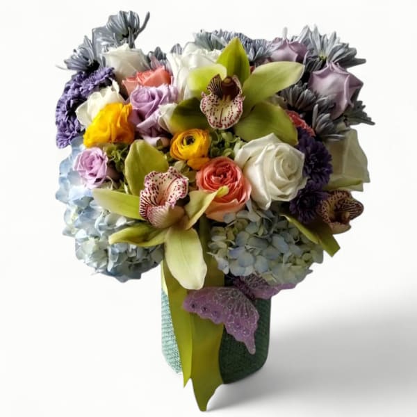 Tall mixed bouquet with orchids, roses, ranunculus, and hydrangeas in a green vase with a butterfly accent.