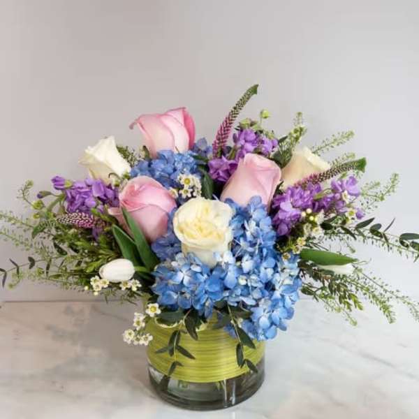 Bouquet of pink roses, blue hydrangeas, and purple flowers in a glass vase