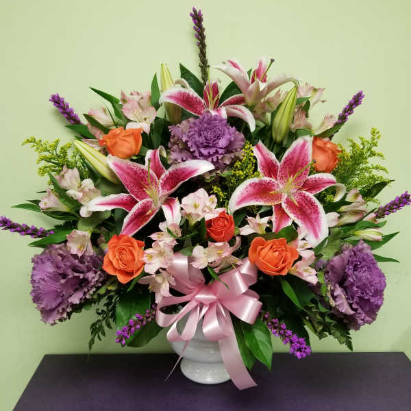 Bouquet of pink lilies, orange roses, and purple flowers in a white vase