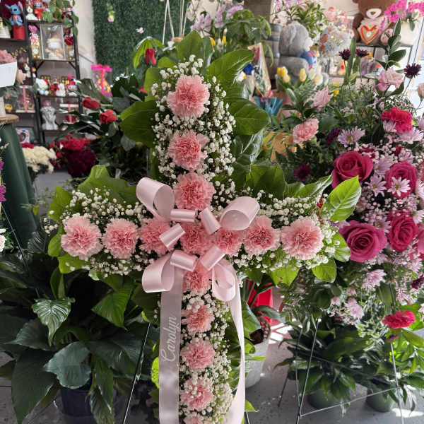 Pink carnation cross on a stand with a ribbon bow