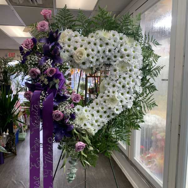 Heart-shaped floral wreath with white daisies and purple roses on an easel