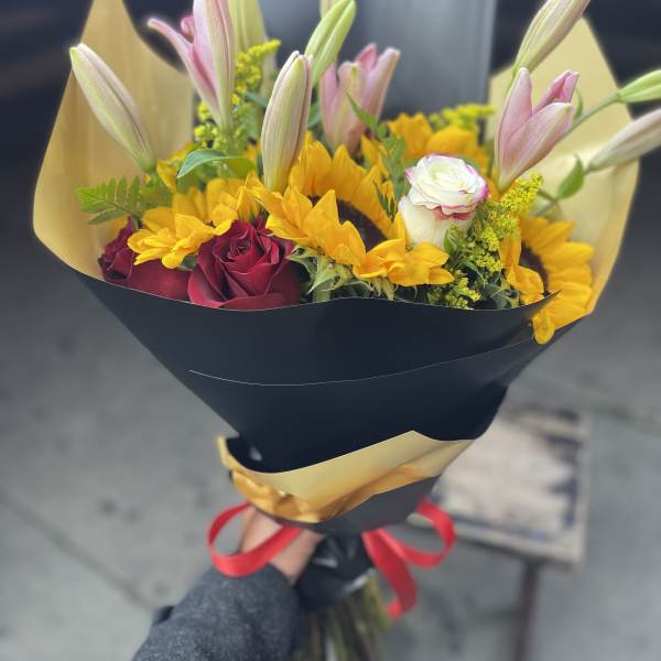 Bouquet of pink lilies, yellow sunflowers, and red roses wrapped in black paper