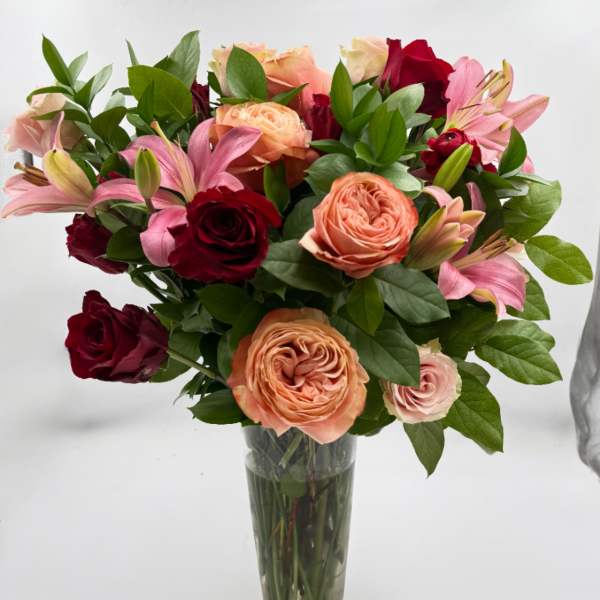 Bouquet of pink, peach, and red roses with lilies in a clear glass vase