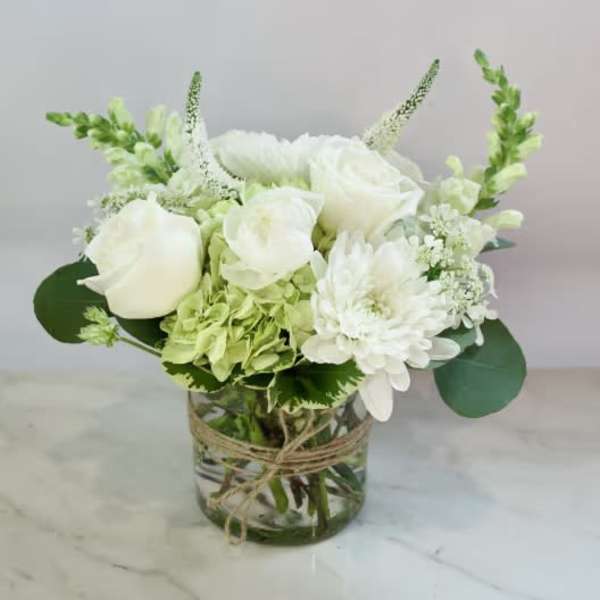 White roses and mums in a glass vase with green accents