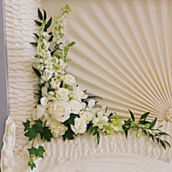 White floral spray arranged on a draped casket with greenery