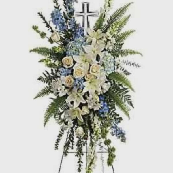 Standing funeral spray with white lilies, blue flowers, and a cross
