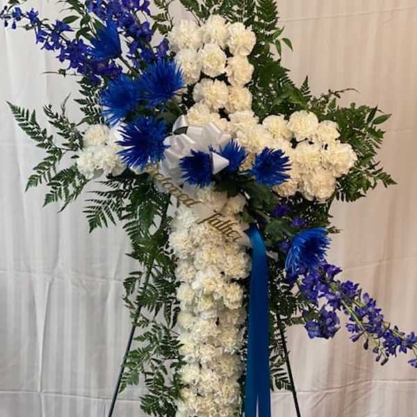 Standing floral spray with white flowers, blue accents, and a ribbon on an easel