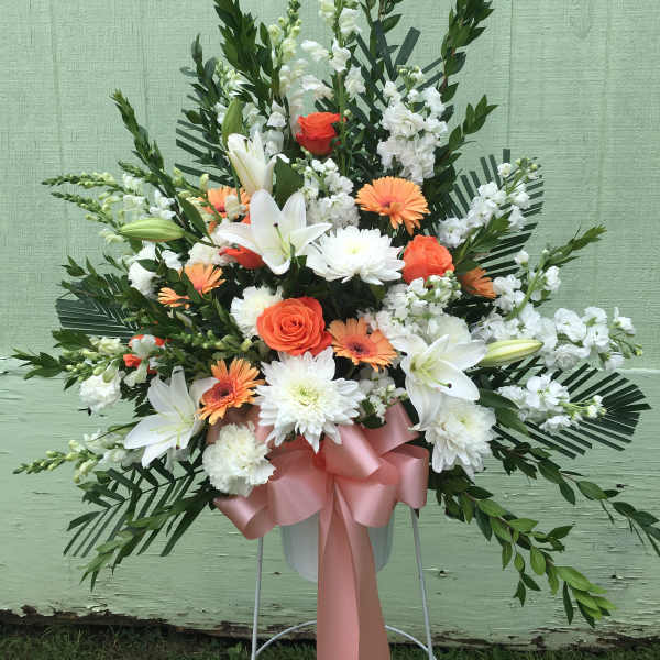 Standing floral spray with white lilies, orange roses, and white daisies
