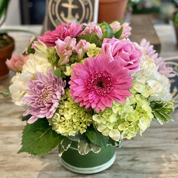 Pink and lavender flowers arranged in a green hatbox