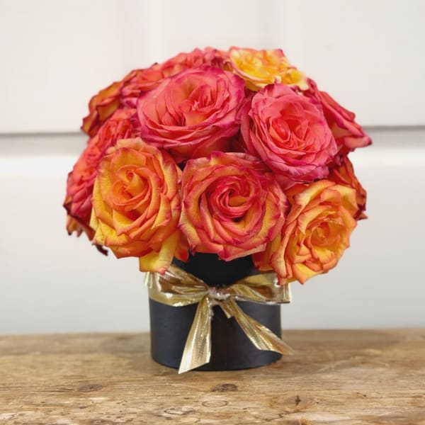 Bouquet of pink and orange roses in a black box tied with a gold ribbon