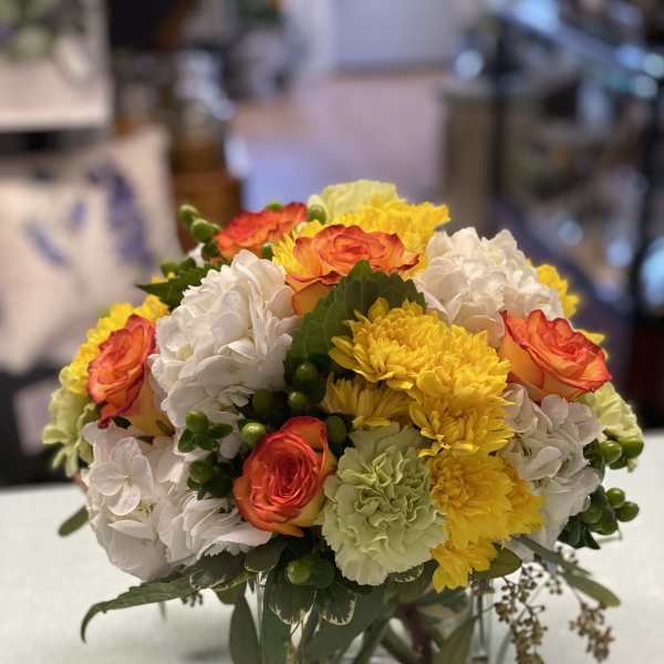 Mixed bouquet of orange roses, white hydrangeas, and yellow chrysanthemums in a glass vase