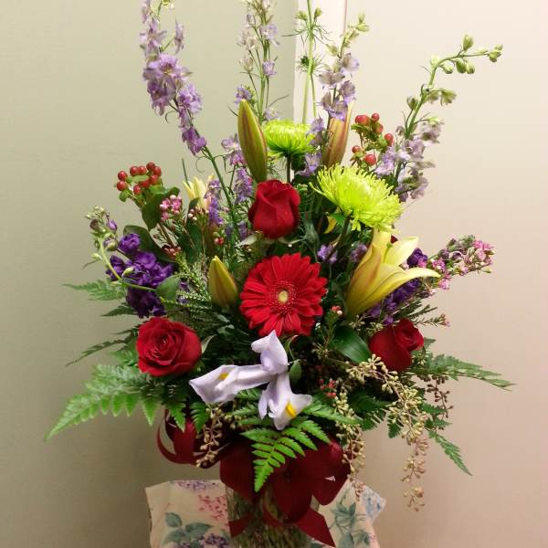 Tall mixed bouquet in a glass vase with red roses, lilies, and purple flowers