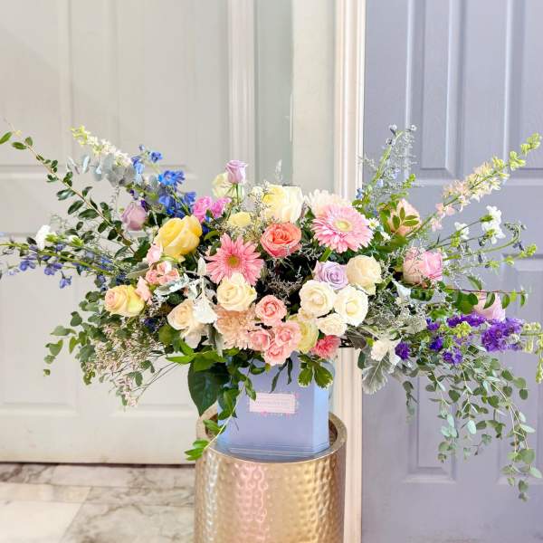 Large pastel bouquet with roses, gerbera daisies, and delphinium in a blue box