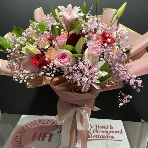 Pink and red mixed bouquet with lilies, roses, and baby's breath wrapped in pink paper