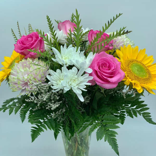 Bouquet of pink roses, white daisies, and yellow sunflowers in a glass vase