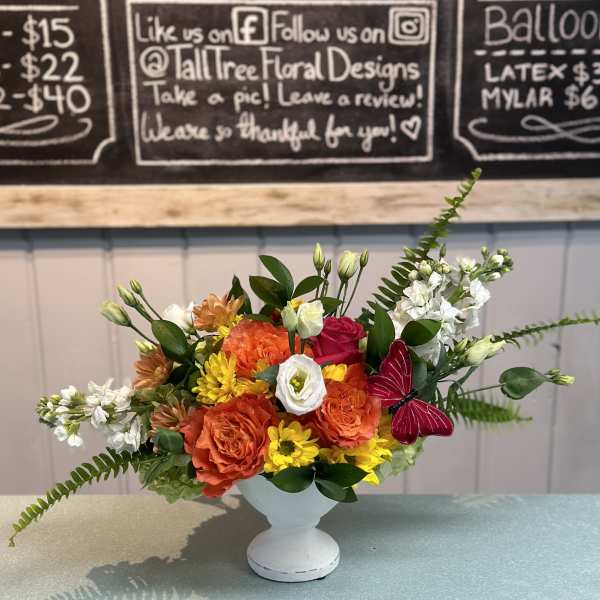 Colorful flower arrangement in a white pedestal vase with a butterfly accent