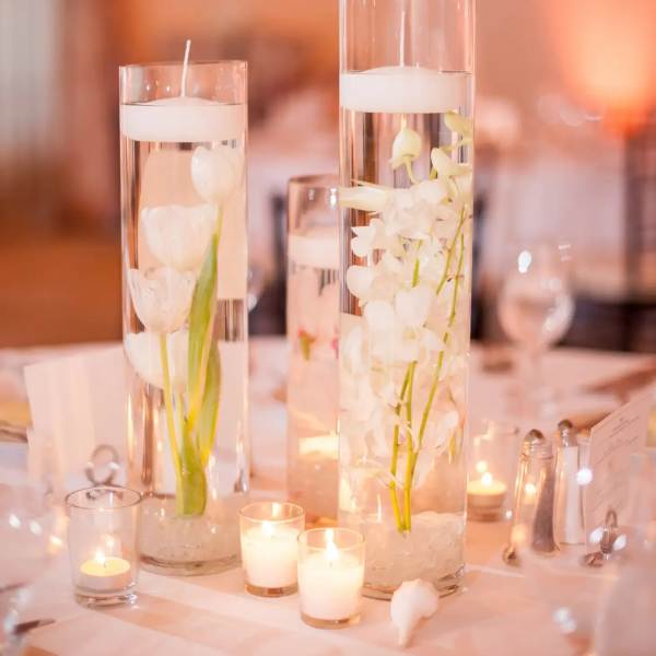 Tall glass vases with white flowers and floating candles on a table