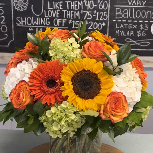 Bouquet of sunflowers, orange roses, and white hydrangeas in a glass vase