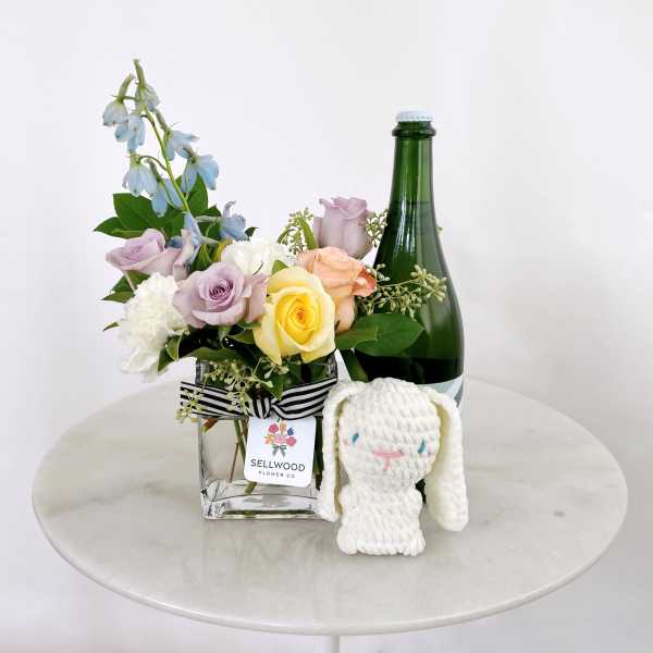 Mixed pastel roses in a glass vase with a plush bunny and bottle