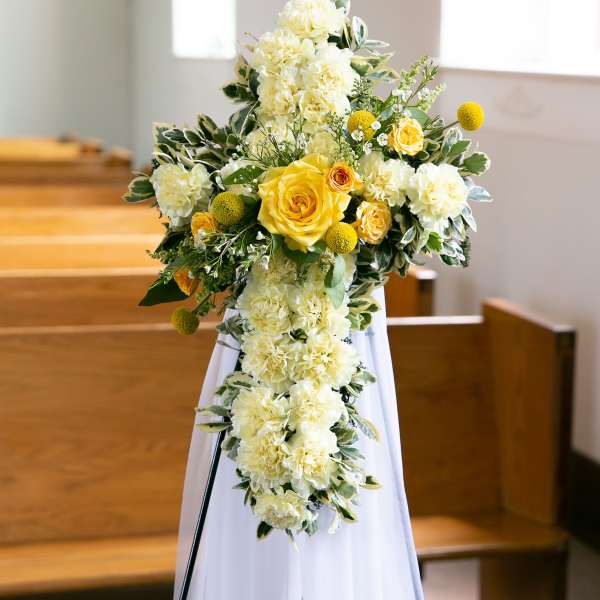 Yellow and white floral cross on a white stand in a church