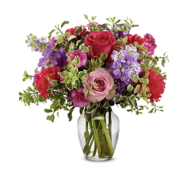 Mixed pink, purple, and red flowers in a clear glass vase