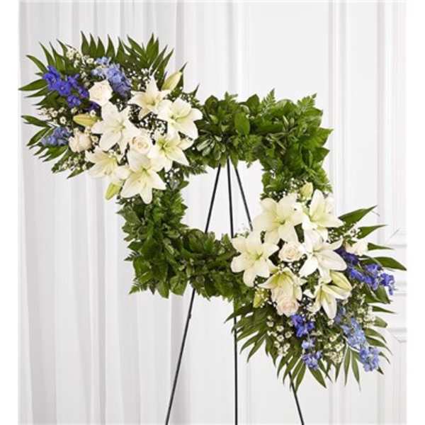 Heart-shaped floral wreath with white lilies and blue flowers on a stand