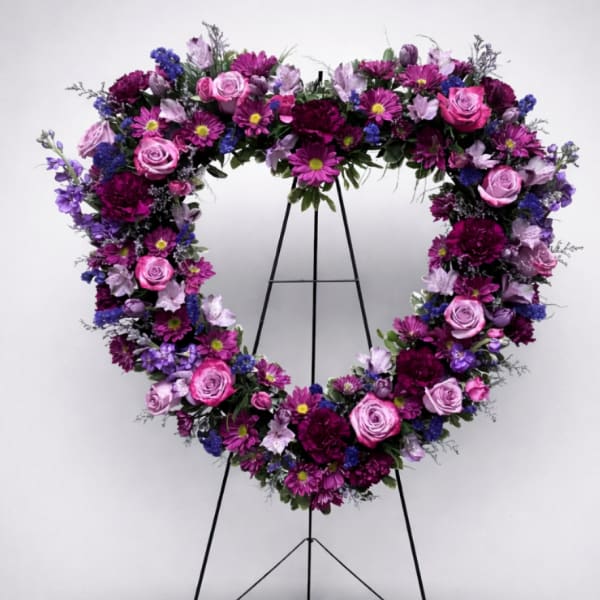 Heart-shaped floral wreath on a black stand with pink, purple, and blue flowers