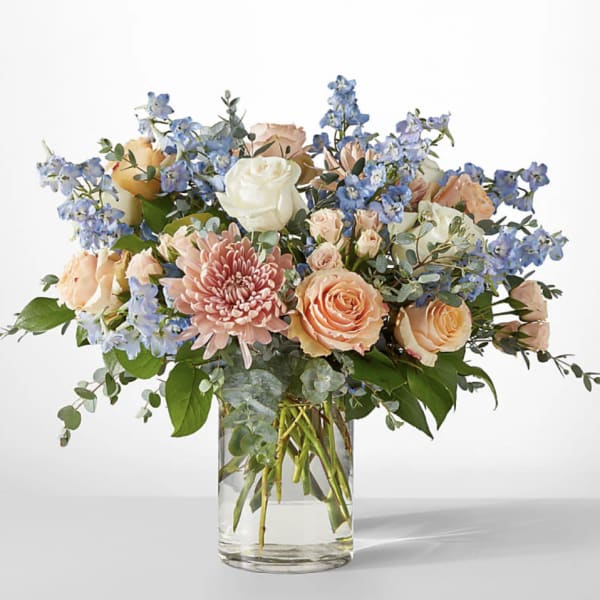 Bouquet of peach and white roses with blue flowers in a glass vase