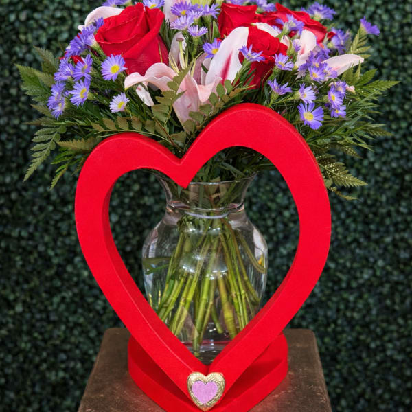 Red roses and pink lilies in a glass vase framed by a red heart