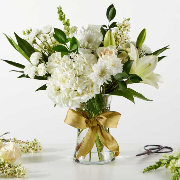 White floral bouquet in a glass vase with a gold ribbon