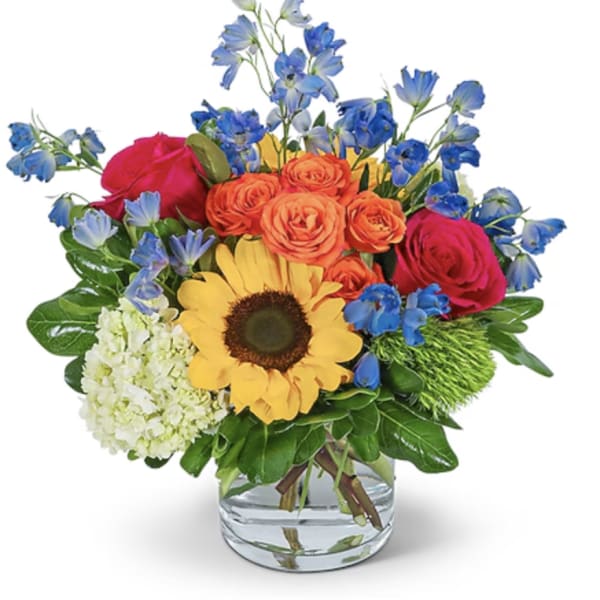 Mixed bouquet with sunflowers, roses, and blue flowers in a glass vase