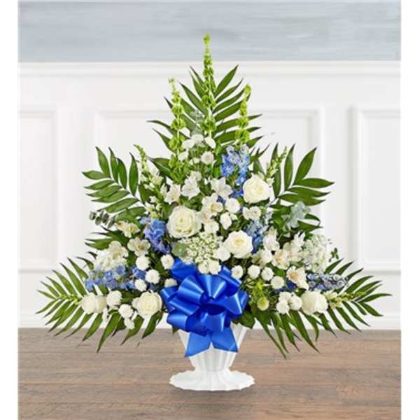 White and blue floral arrangement in a white pedestal vase with a blue bow