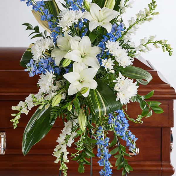 White lilies and blue flowers in a standing funeral spray