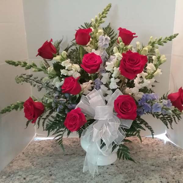 Red rose arrangement in a white vase with a sheer ribbon