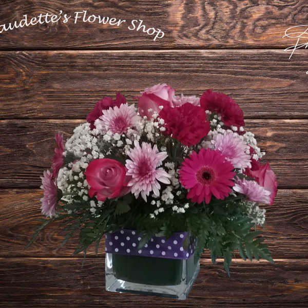 Pink mixed flower arrangement in a square glass vase with a polka-dot ribbon