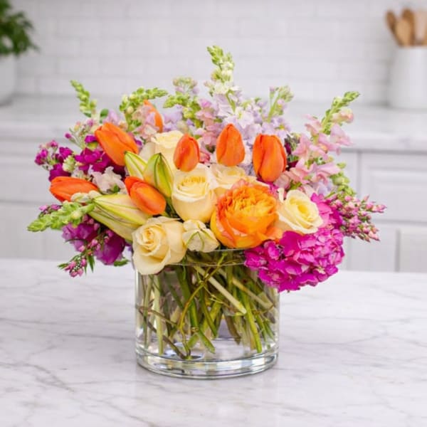 Mixed bouquet of orange tulips, cream roses, and pink flowers in a glass vase