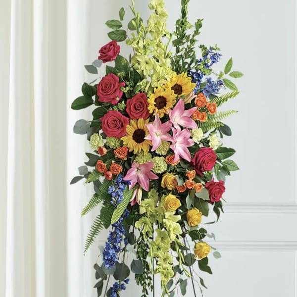 Tall floral standing spray with roses, lilies, sunflowers, and blue accents