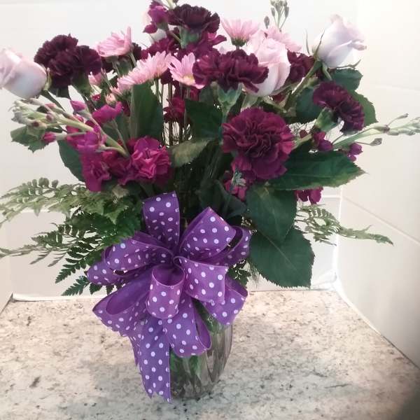 Purple and pink mixed flower bouquet in a glass vase with a polka-dot ribbon