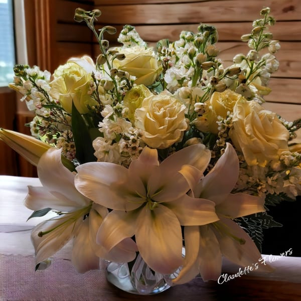 Cream roses and white lilies arranged in a clear glass vase