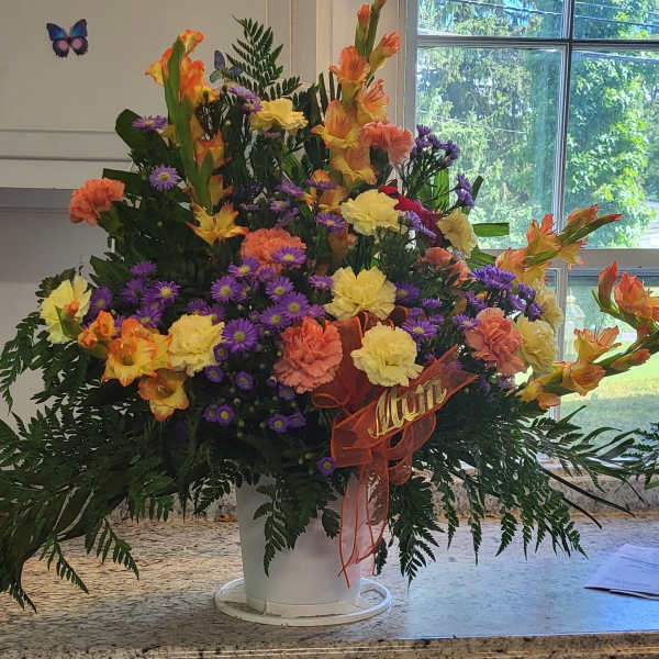 Colorful mixed flower arrangement in a white bucket with a ribbon