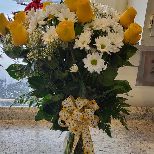 Yellow roses and white daisies in a clear glass vase with a yellow ribbon